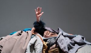 Hand reaching out from a large pile of clothes, symbolising wardrobe overwhelm and the need for a detox